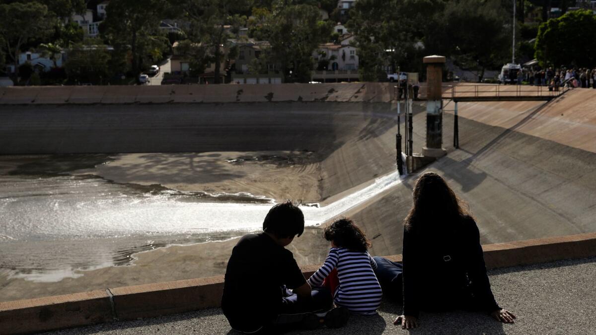 A family watches as water flows into the Silver Lake Reservoir complex. Officials on Tuesday began the process of refilling the 96-acre Silver Lake and Ivanhoe reservoirs.