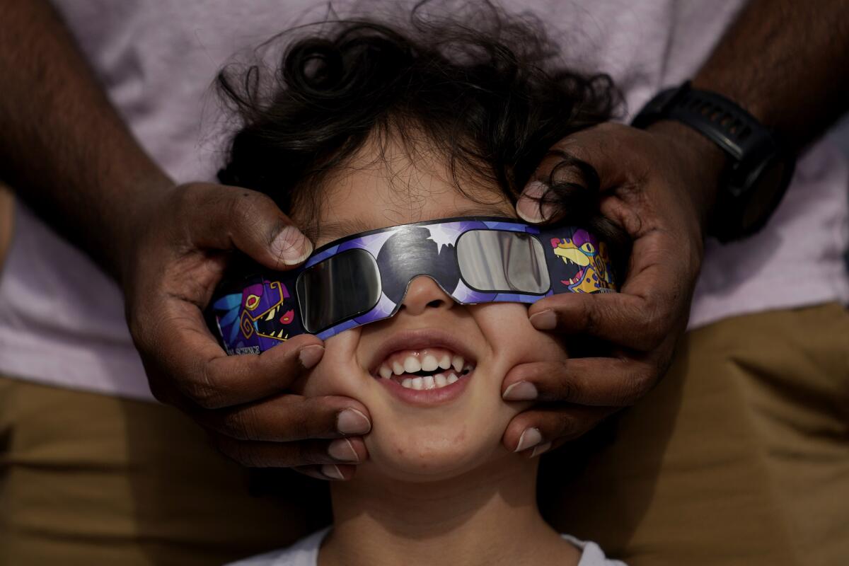A man holds special sunglasses over the eyes of a boy.