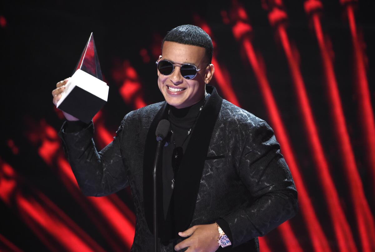 A man wearing a suit and sunglasses hold up a music trophy