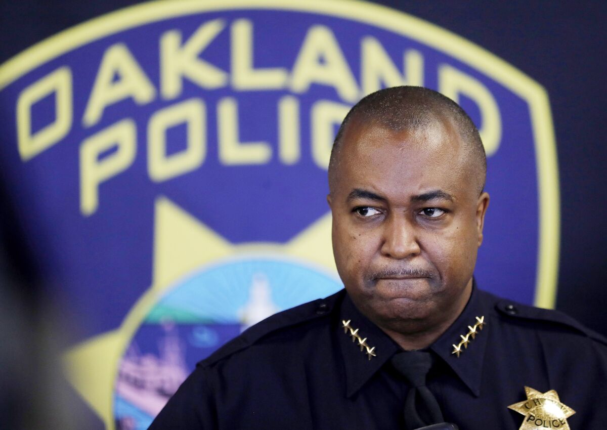 A man in police uniform stands in front of a backdrop that says "Oakland Police."