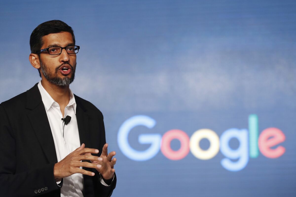 Google CEO Sundar Pichai speaks in front of a screen with the Google logo on it.