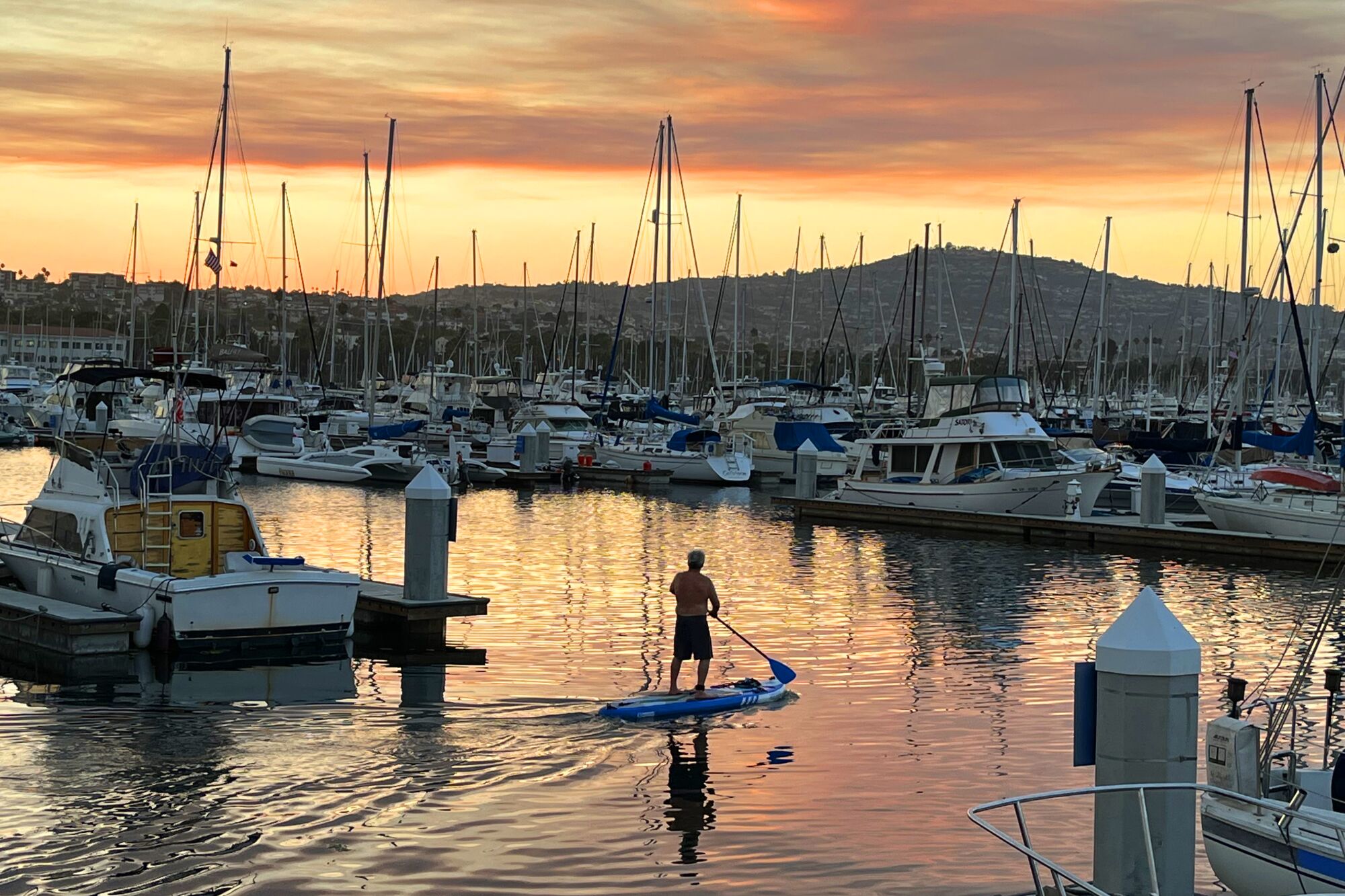 A padddle baorder in the San Pedro marina under a smoky sunset, due to the wildfires in Southern California