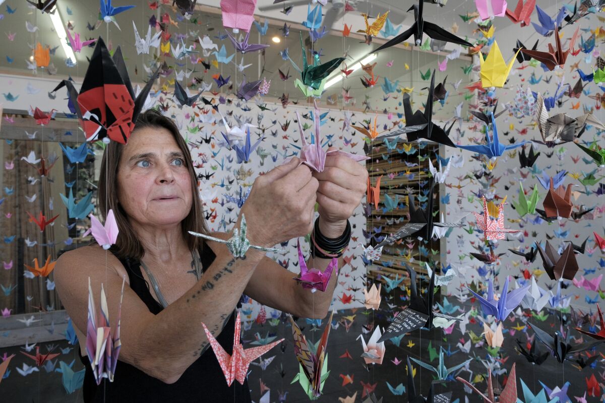 Artist Karla Funderburk, owner of Matter Studio Gallery, adjusts one of of the thousands of origami cranes hanging during an exhibit honoring the victims of COVID-19, Tuesday, Aug. 11, 2020, in Los Angeles. Funderburk started making the cranes three months earlier, stringing the paper swans in pink, blue, yellow and many other colors together and hanging them in her gallery. (AP Photo/Richard Vogel)