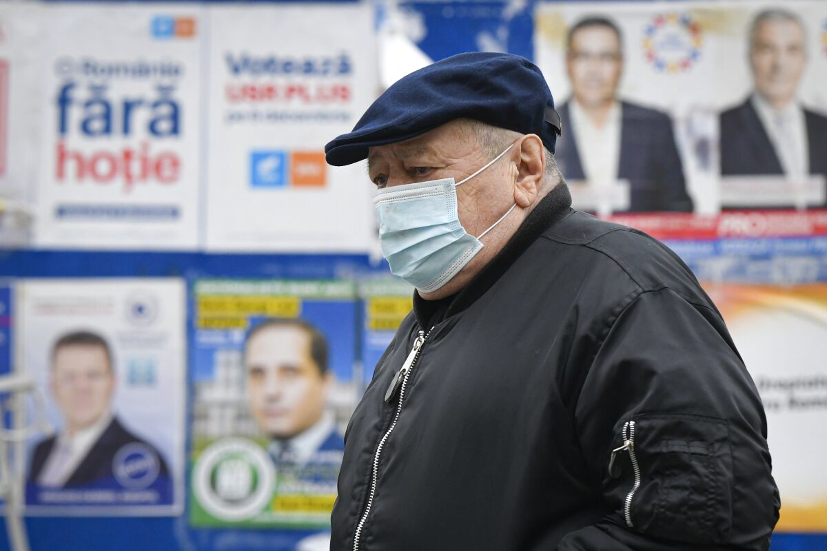 A man wearing a mask for protection against the COVID-19 infection walks by electoral posters in Bucharest, Romania, Thursday, Dec. 3, 2020. Romania will hold parliamentary elections on Sunday Dec. 6. (AP Photo/Andreea Alexandru)