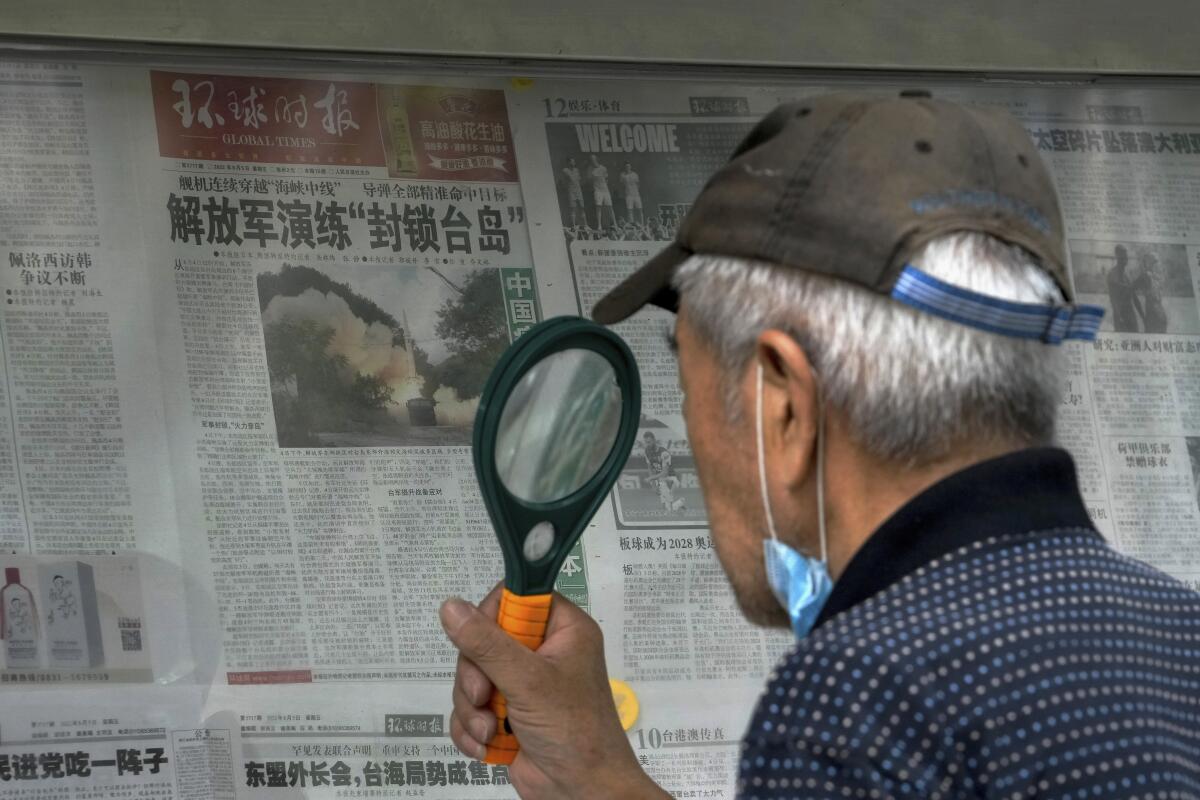A man uses a magnifying glass to read a newspaper headline.