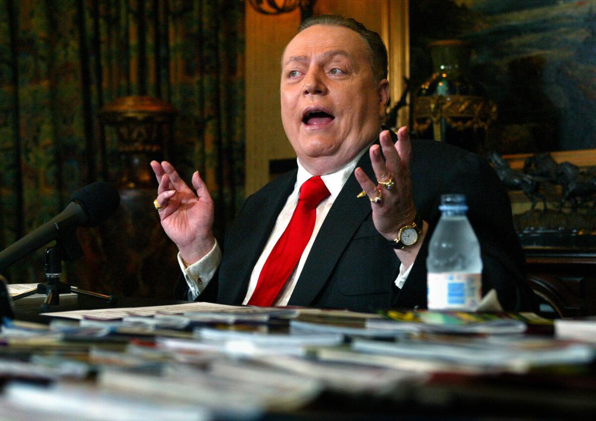 Larry Flynt, in red tie, speaks before a microphone