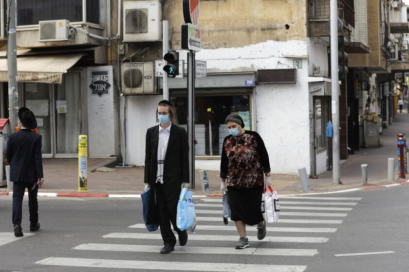 Ultra-Orthodox Jews wearing protective masks walk by carrying bags of shopping in the religious Israeli city of Bnei Brak, near Tel Aviv, on April 6, 2020, during the novel coronavirus pandemic crisis. - More than 7,000 cases of COVID-19, including 40 deaths, have been officially declared in Israel, half of which according to local media, are ultra-Orthodox Jews, prompting the Prime Minister on April 3, to give a green light for amry deployment in the city, considered the centre of the country's novel coronavirus outbreak. (Photo by MENAHEM KAHANA / AFP) (Photo by MENAHEM KAHANA/AFP via Getty Images)