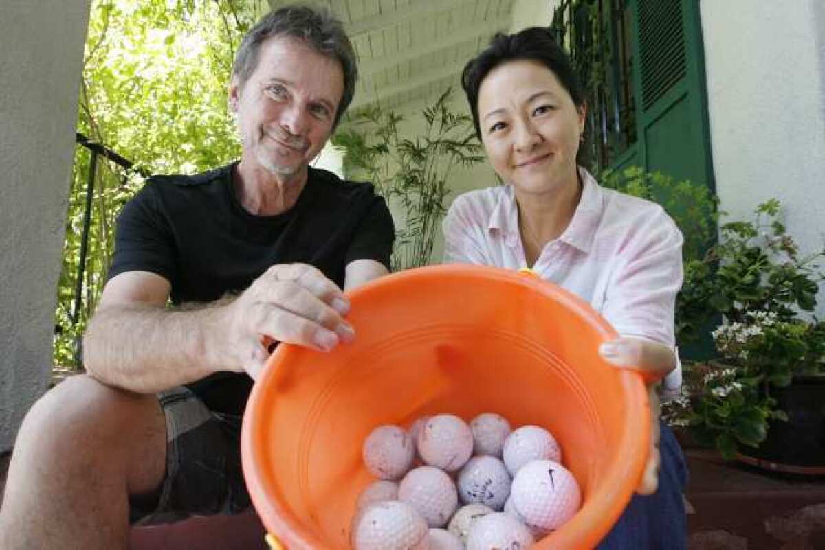 Neighbors Edward Bash and Suzie Nelson hold a bucket of golf balls that have been hit from Oakmont Country Club onto their side of the street.