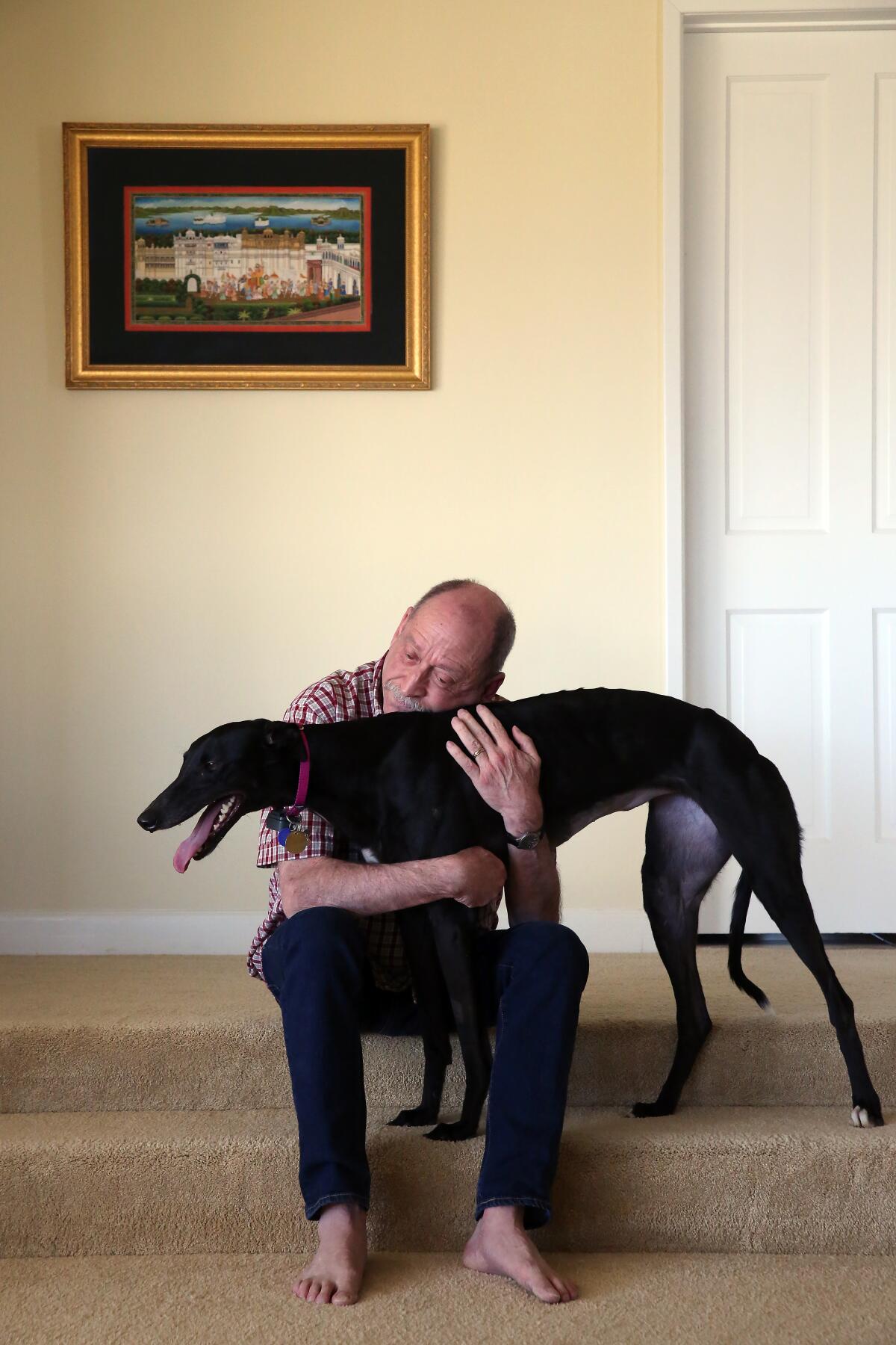 Tim Lignoul, sitting on carpeted steps, hugs his greyhound Vicky,