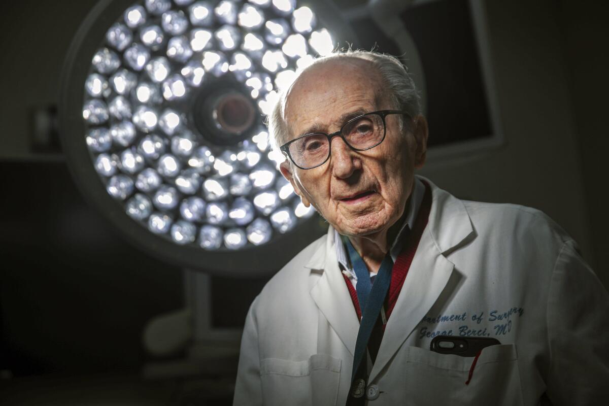 A surgeon stands under surgical lamps