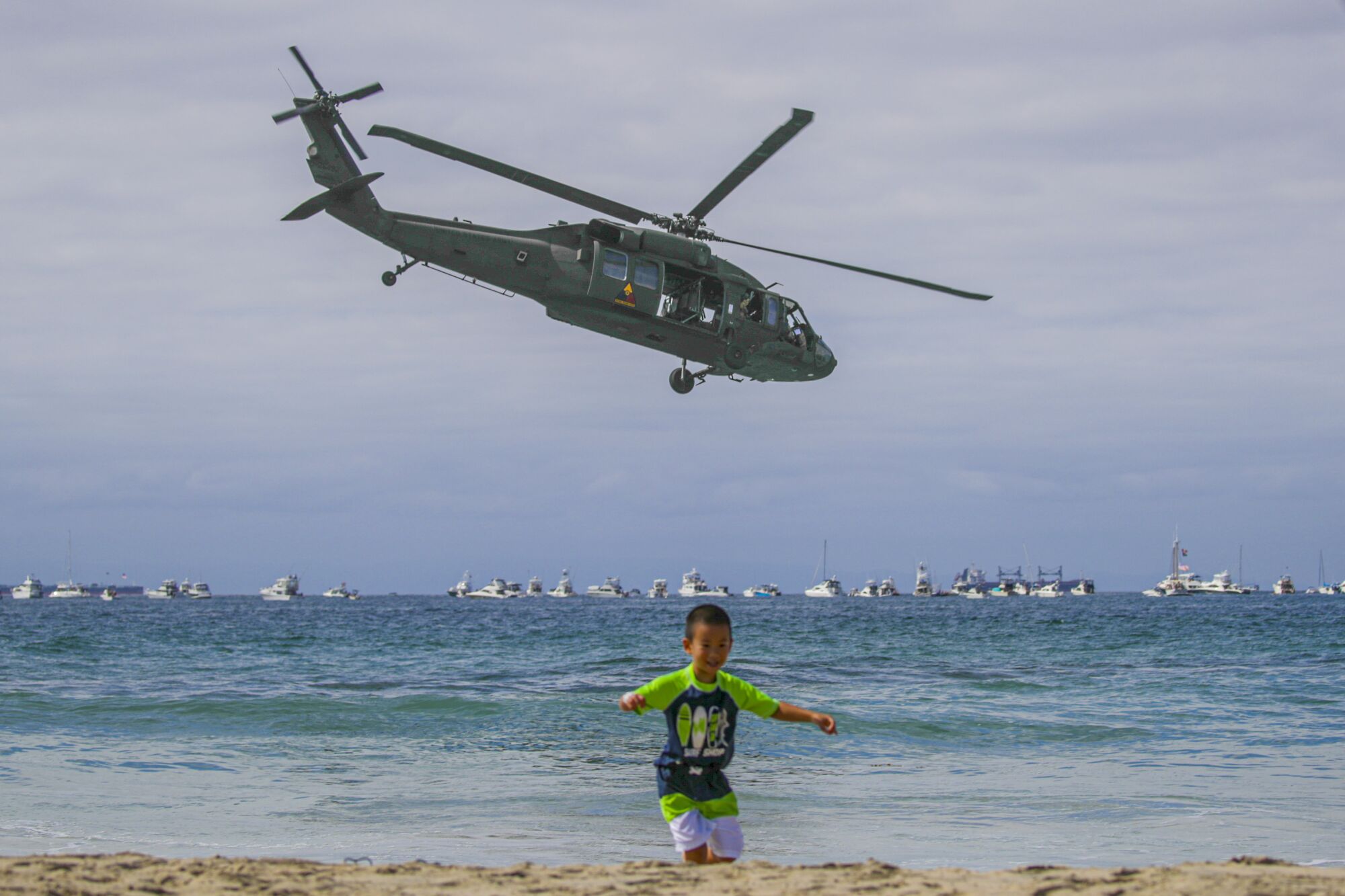 A child plays on the beach as a U.S. Army UH60 Blackhawk helicopter looms 