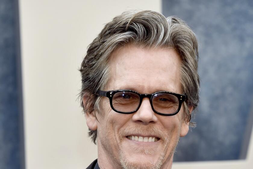 Kevin Bacon in dark sunglasses and a black suit and tie