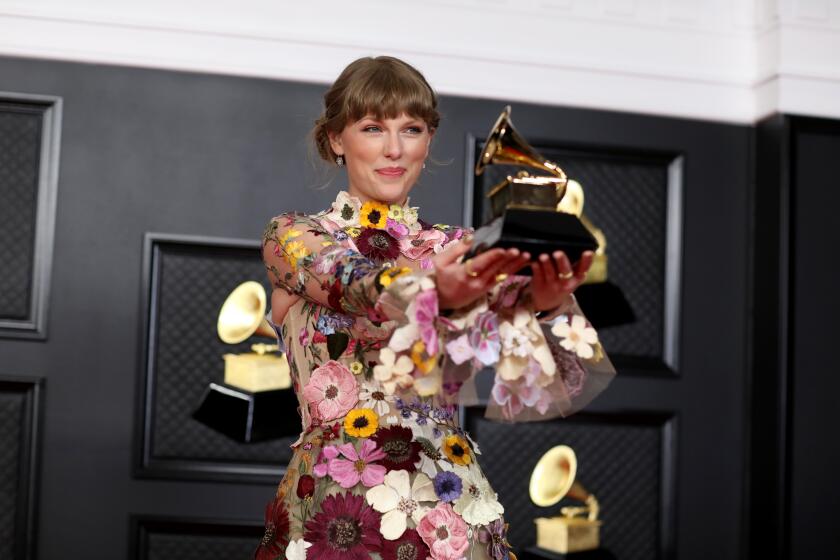 Taylor Swift holding her Grammy trophy on a red carpet
