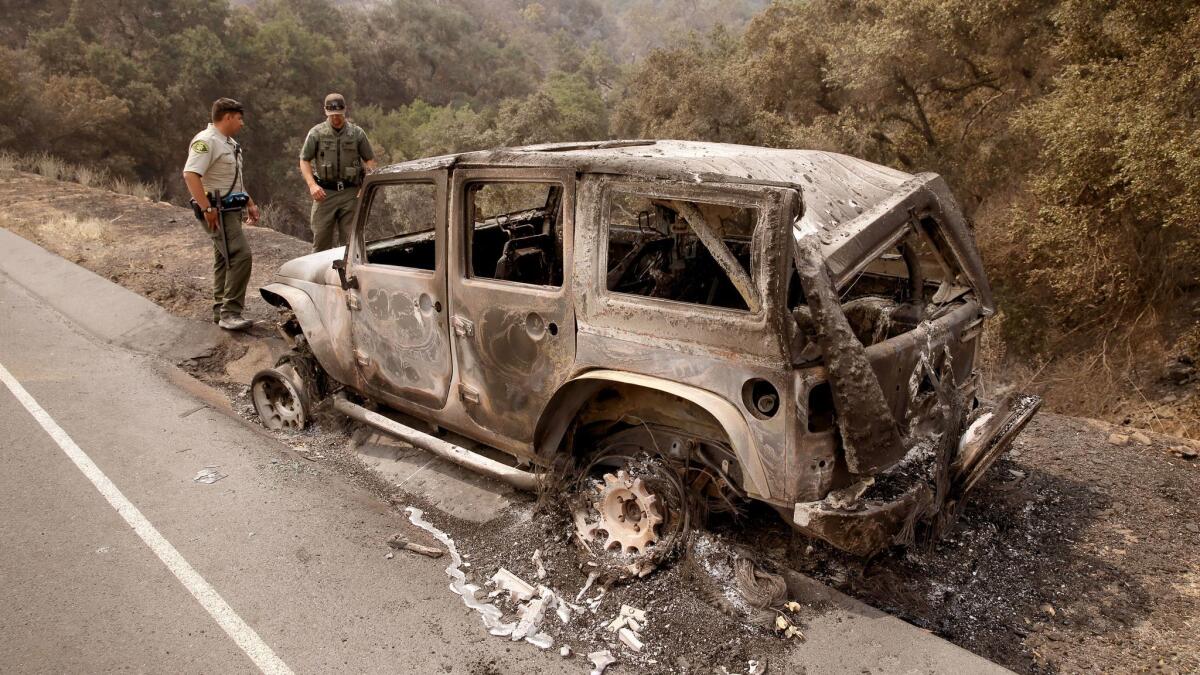 Santa Barbara County Sheriff's Deputy B. Bruening, left, and U.S. Fish and Wildlife warden Max Magleby inspect a Jeep that was abandoned and scorched by the Whittier fire along Highway 154.