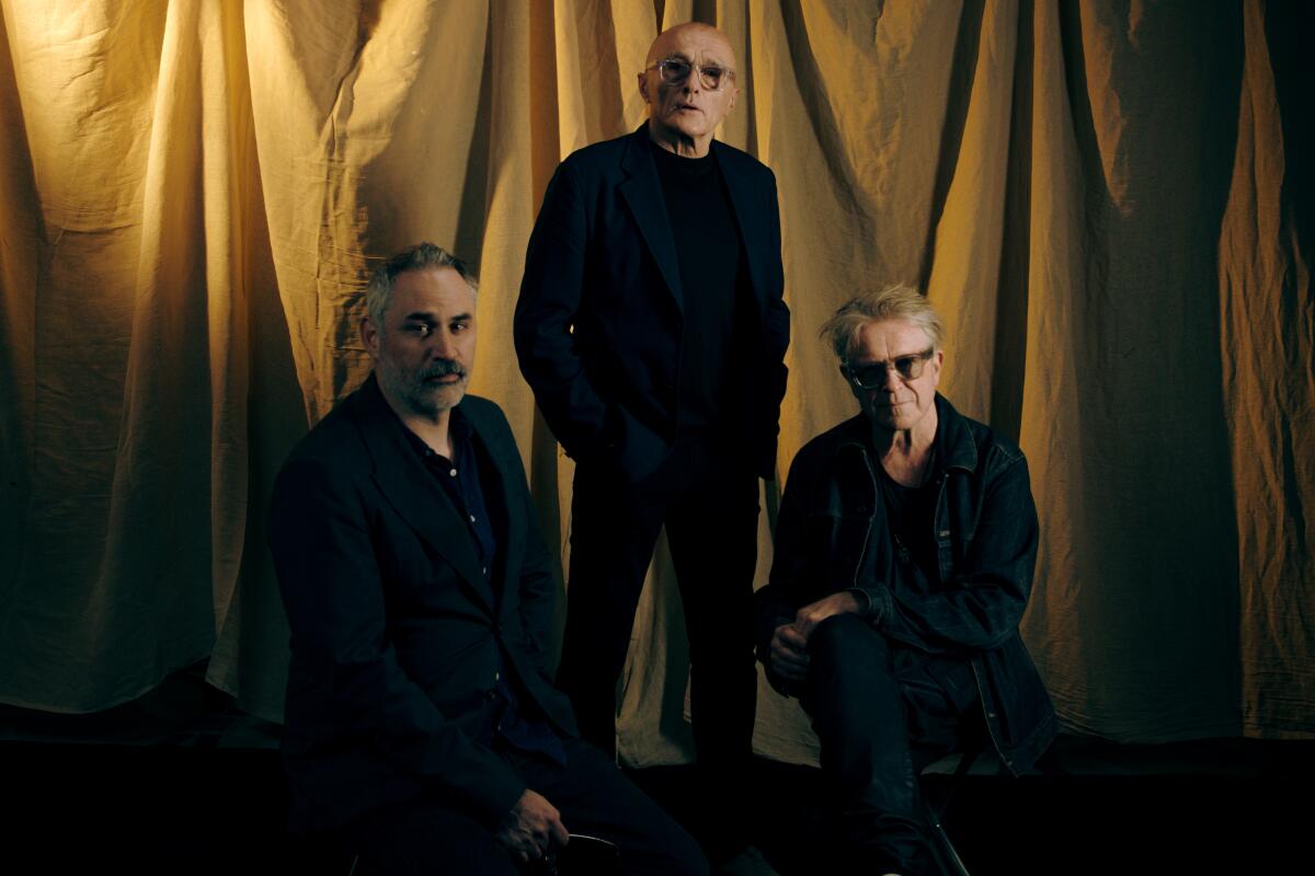 Three film collaborators pose in front of a gold curtain.