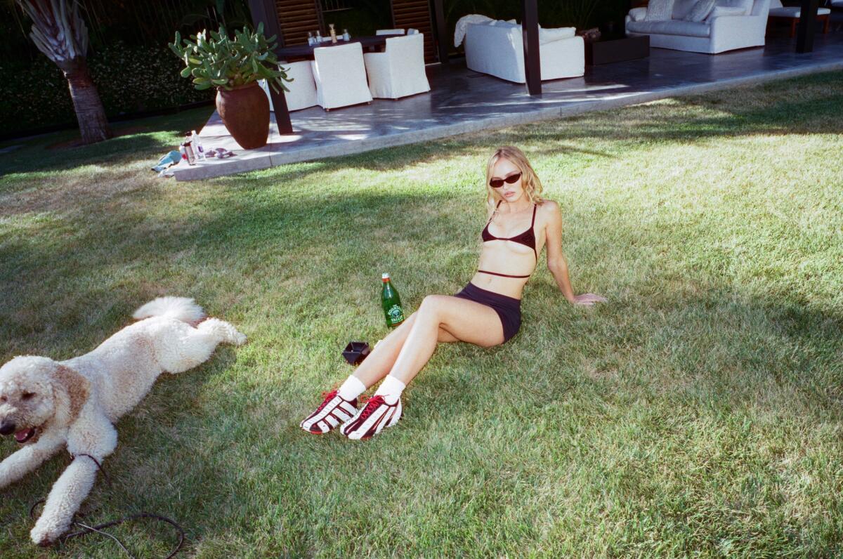 A woman in a black bikini reclines on the grass next to a large dog.