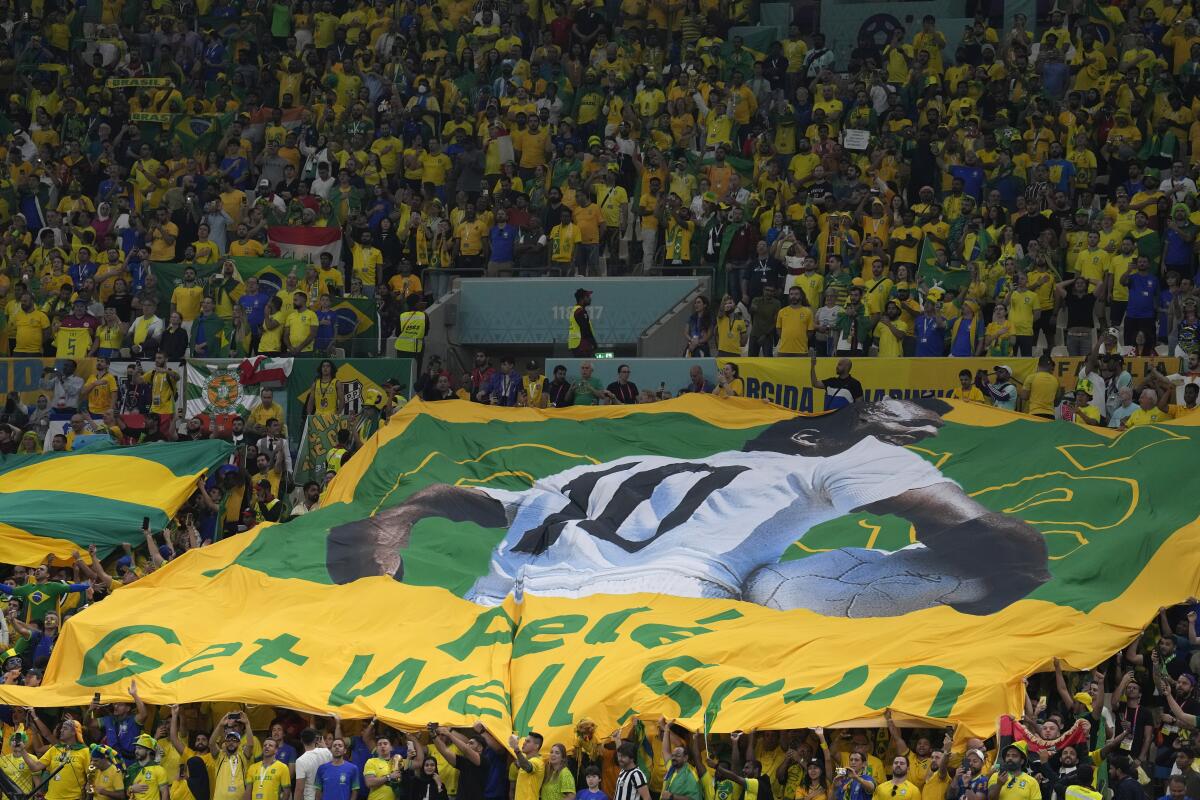 Brazilian fans hold a giant Brazilian flag with picture of former Brazilian player Pele with message reads in English "Pele, Get well soon," during the World Cup group G soccer match between Cameroon and Brazil, at the Lusail Stadium in Lusail, Qatar, Friday, Dec. 2, 2022. (AP Photo/Natacha Pisarenko) :