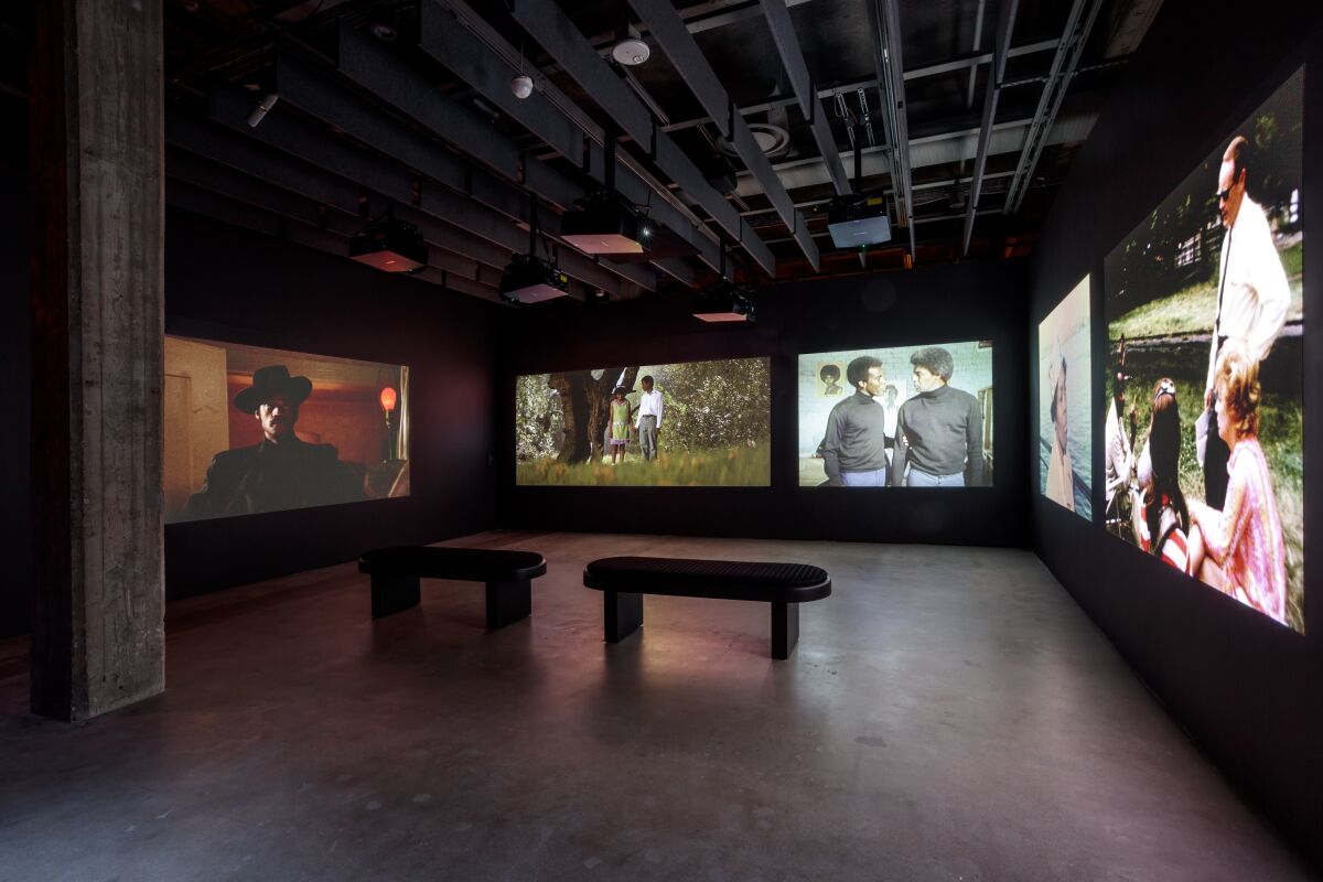 A museum exhibit features a darkened room with film scenes on large lighted screens.