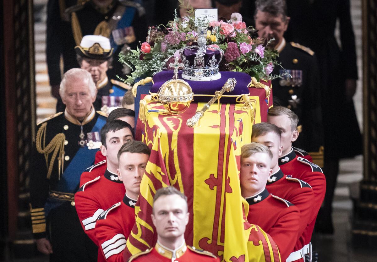 King Charles III walks beside the coffin of Queen Elizabeth II, carried by men in military uniform, at Westminster Abbey.