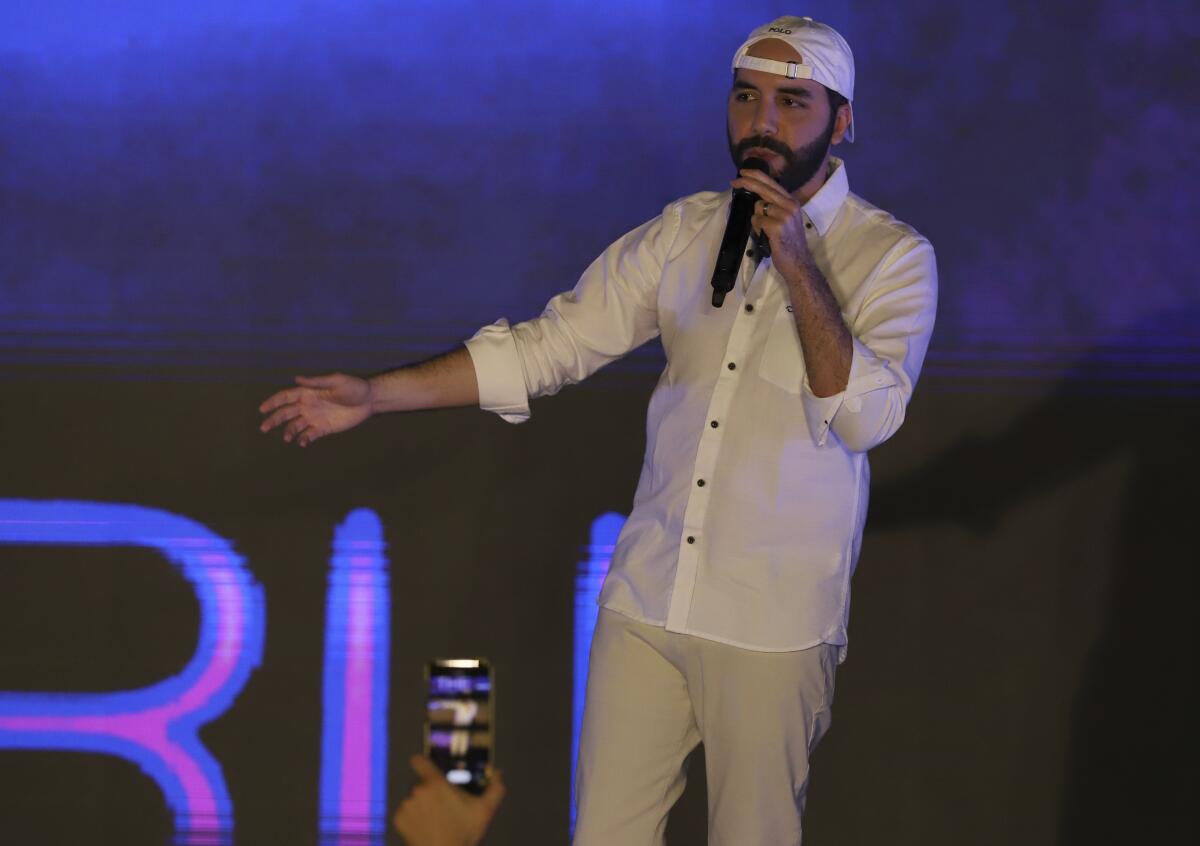 Salvadoran President Nayib Bukele speaking from a stage in shirtsleeves and a backward baseball cap