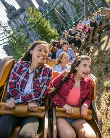 Guests ride a roller coaster with a castle in the background