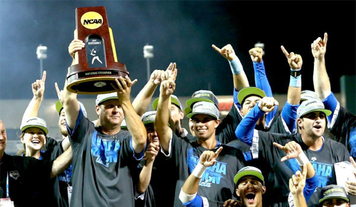 UCLA Coach John Savage, left, holds the Bruins' first baseball championship trophy after defeating Mississippi State, 8-0, to win the College World Series.