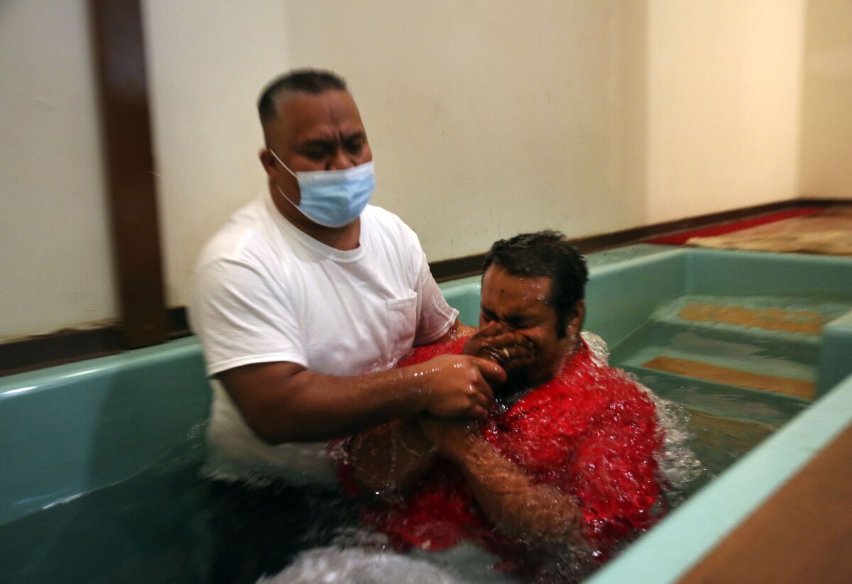 Pastor Luke Jesse of the First Marshallese Throne in Jouj church wears a mask as he baptizes Danny Baro on Sunday, Nov. 22, 2020, in Noel, Mo. After the coronavirus swept through the town of about 1,800 people, the First Marshallese Throne in Jouj and four other churches that worship at the building of the Community Baptist Church experienced a faith revival with an estimated 50 baptisms in three months. (AP Photo/Jessie Wardarski)