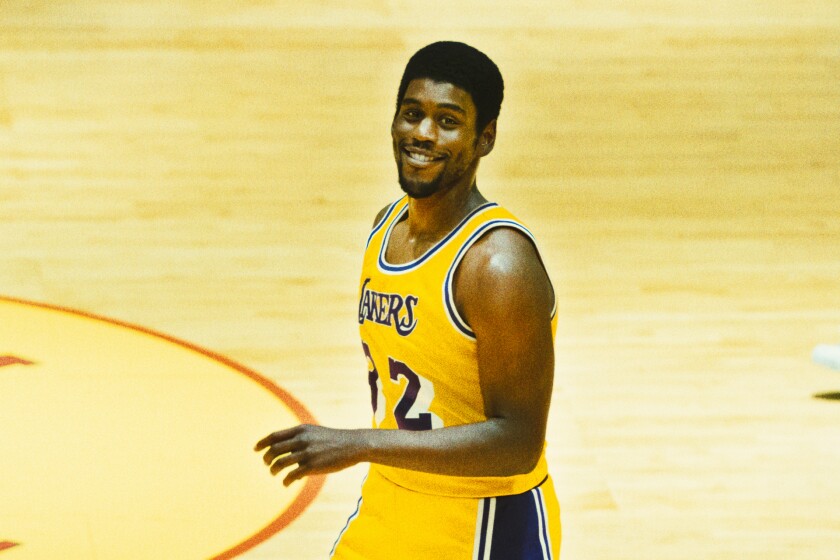 An actor portraying Lakers star “Magic” Johnson smiles for the camera as he strolls down the court
