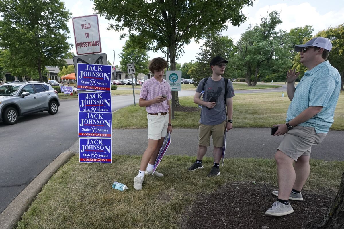 A man talks to two young men next to campaign signs that say "Jack Johnson"