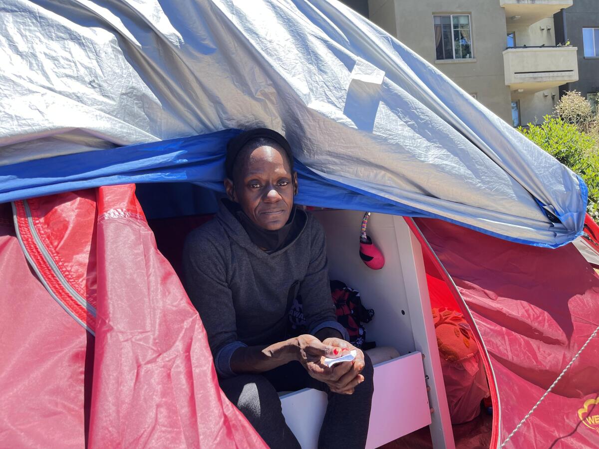 A woman looks out from the opening of a tent.