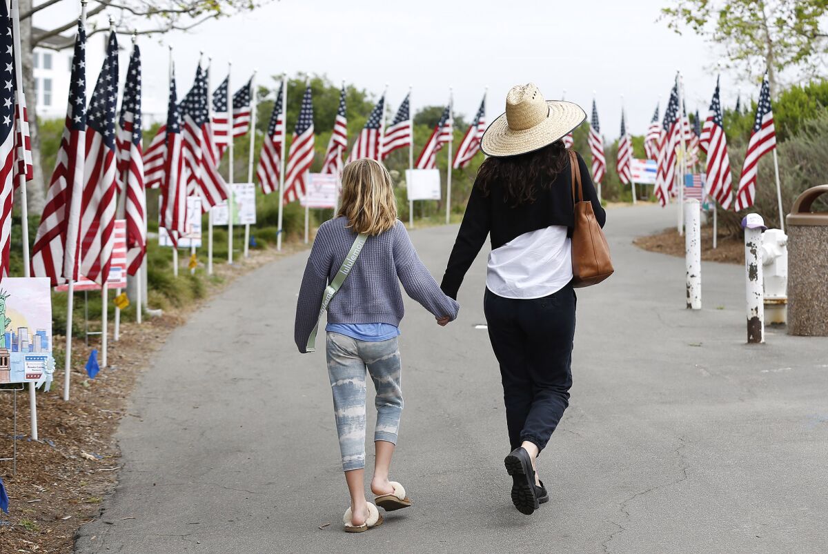 A mother and daughter walk between rows of American flags posted on the pathways.