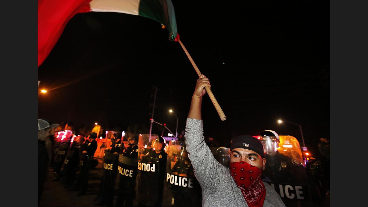A protester waves a flag before a phalanx of police officers in riot gear.
