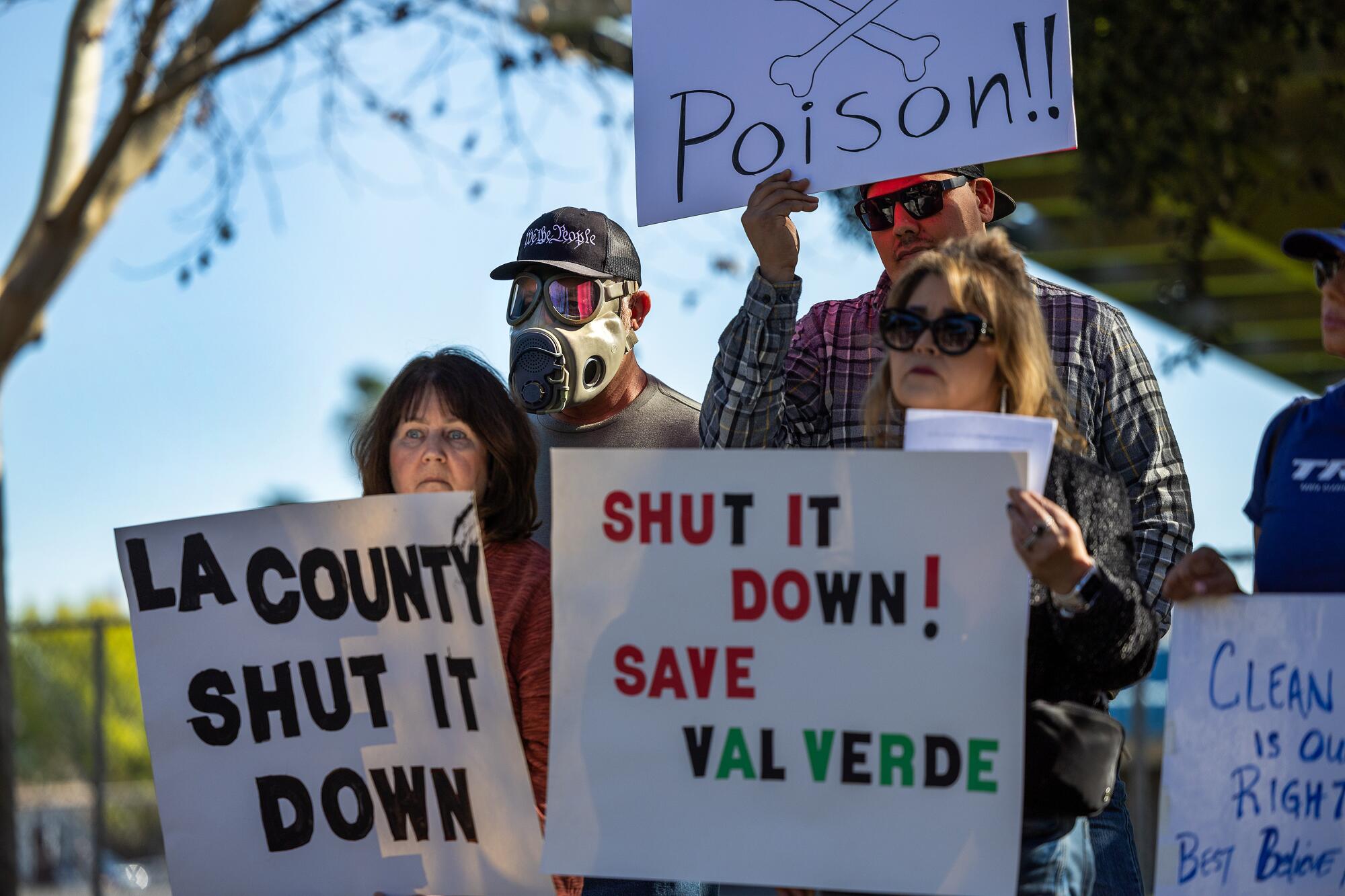 Protesters, one wearing a gas mask, hold signs that read "Poison!!" and "Shut it down! Save Val Verde."