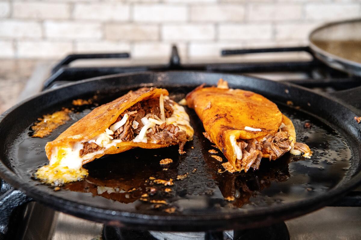 Tacos with meat and melting cheese sit in a skillet