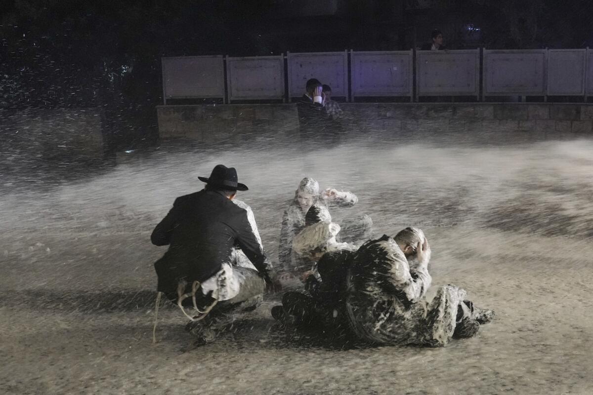 Several people sit while a white liquid is sprayed at them outside in the dark.