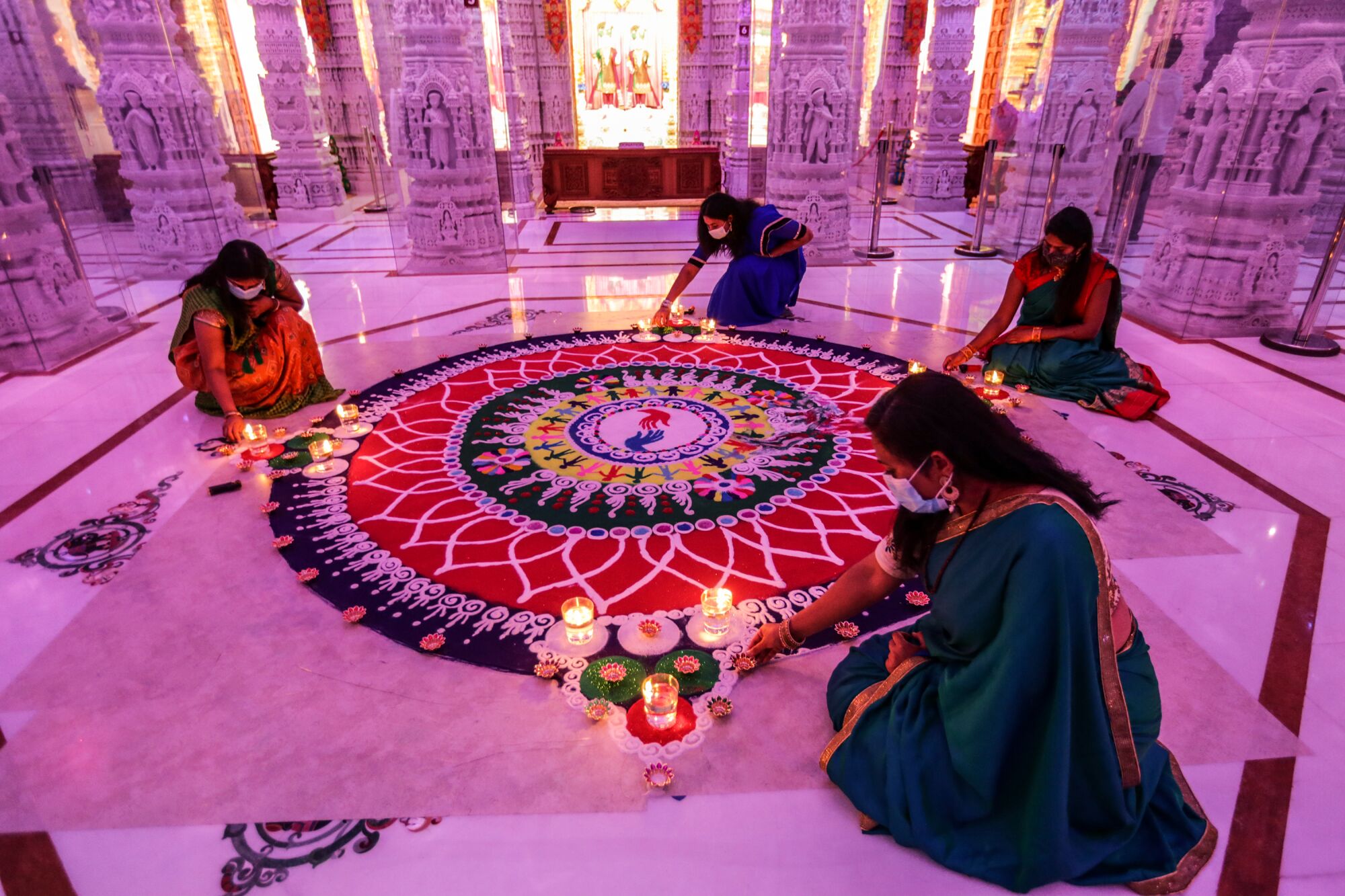 Women in traditional robes kneel around an intricate work of sand art inside a Hindu temple