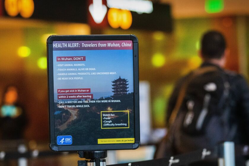 A passenger walks past a sign showing a health alert on the coronavirus near a security checkpoint at Washington state's Sea-Tac International Airport, Wednesday, Jan. 29, 2020. (Ellen M. Banner/The Seattle Times via AP)