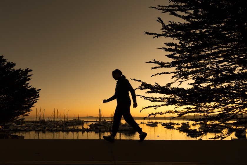 A woman walks on a trail adjacent to the scenic Monterey harbor. 