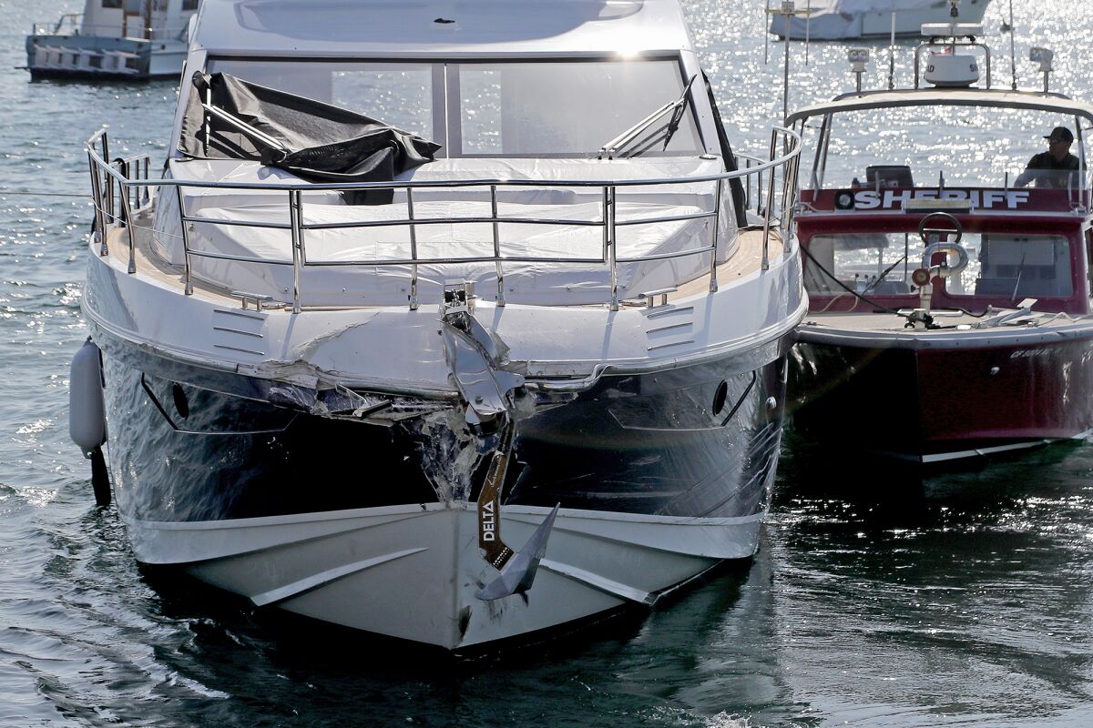 A yacht with damage to its front end is pulled by a sheriff tugboat