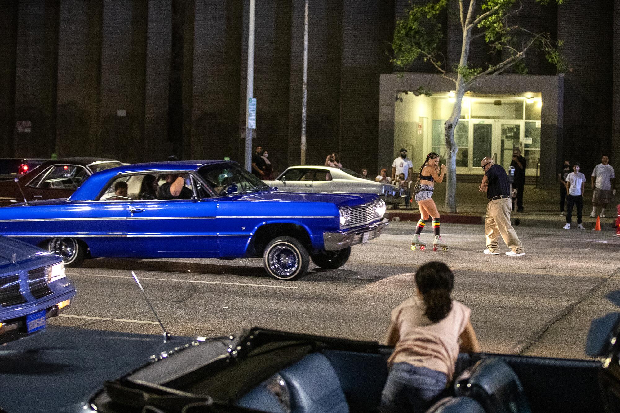 Karla Ramirez, 8, sits in her family's 1963 Chevrolet Impala Super Sport watching a man and a roller skater dance 