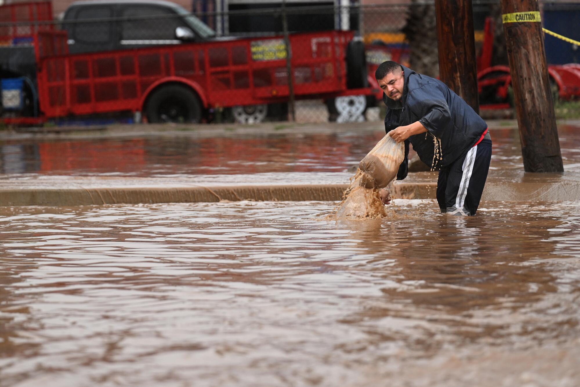A man stands knee-deep in muddy floodwater as he tries to clear a drain.