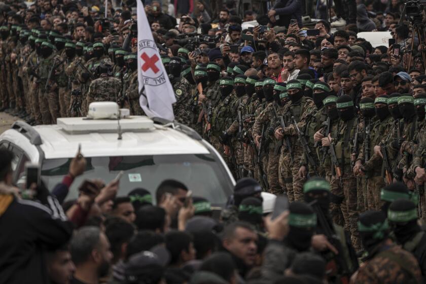 Red Cross vehicles wait as Hamas fighters stand in formation ahead of a hostages release in Deir al-Balah, central Gaza Strip, Saturday Feb. 8, 2025. (AP Photo/Abdel Kareem Hana)