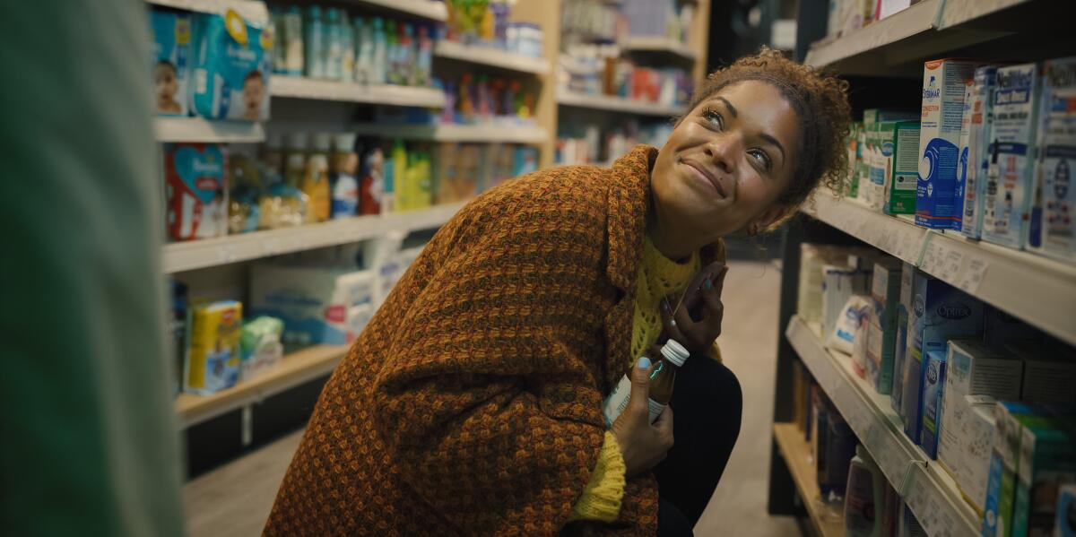 A woman in a brown sweater leans over and smiles up at somebody in a store.