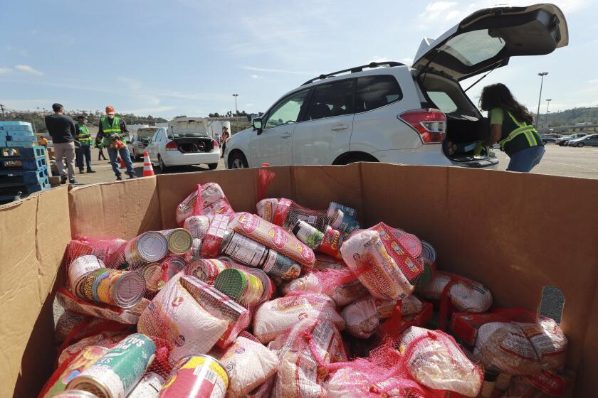 Bags of food items sit in large cardboard bins as volunteers place food into the back of cars during the Mass Emergency Food Distribution, put on by the San Diego and Imperial counties Labor Counsel and the San Diego Food Bank, at SDCCU Stadium on Saturday March 28, 2020 in San Diego, California.