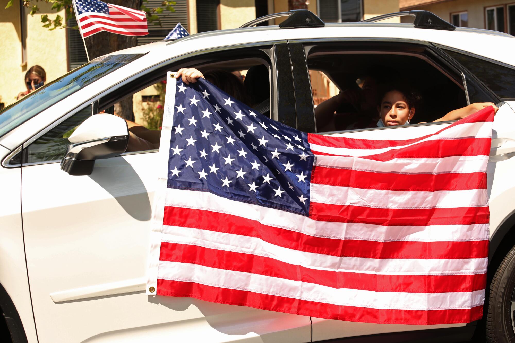 A driver and passenger hold the U.S. flag while joining a parade to honor World War II veteran Lt. Col. Sam Sachs in Lakewood on April 26. 