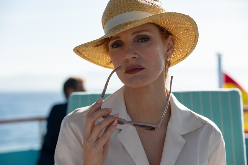 A woman in a sun hat holds her sunglasses while on a boat