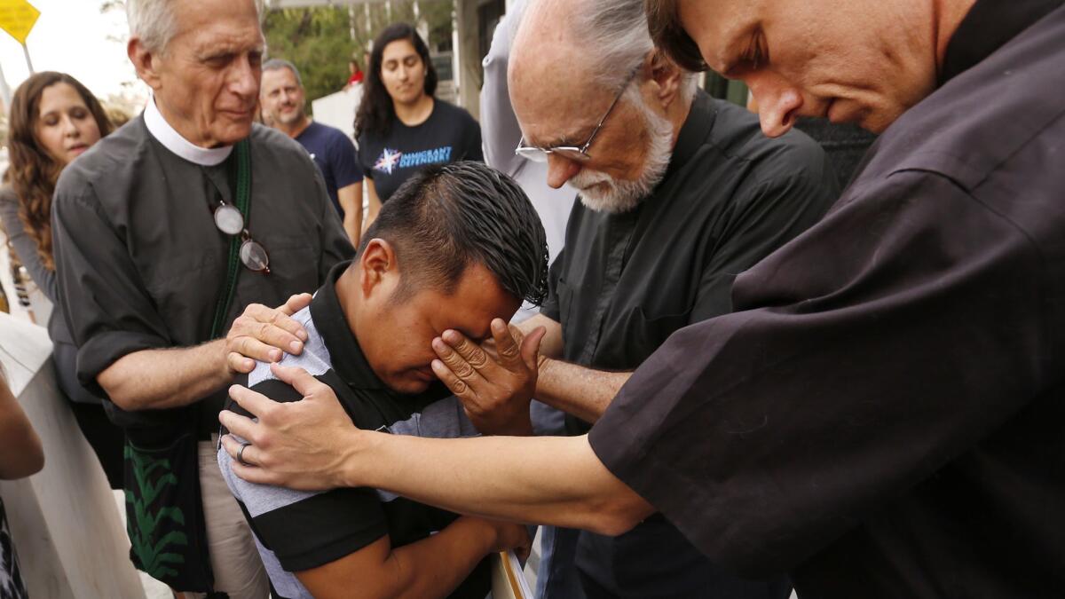 Guatemalan asylum seeker Hermelindo Che Coc, 31, with Father Tom Carey, Rev David Farley, and Rev Matthias Peterson-Brandt, left to right, as they pray outside the Los Angeles Federal Building prior to an hearing.