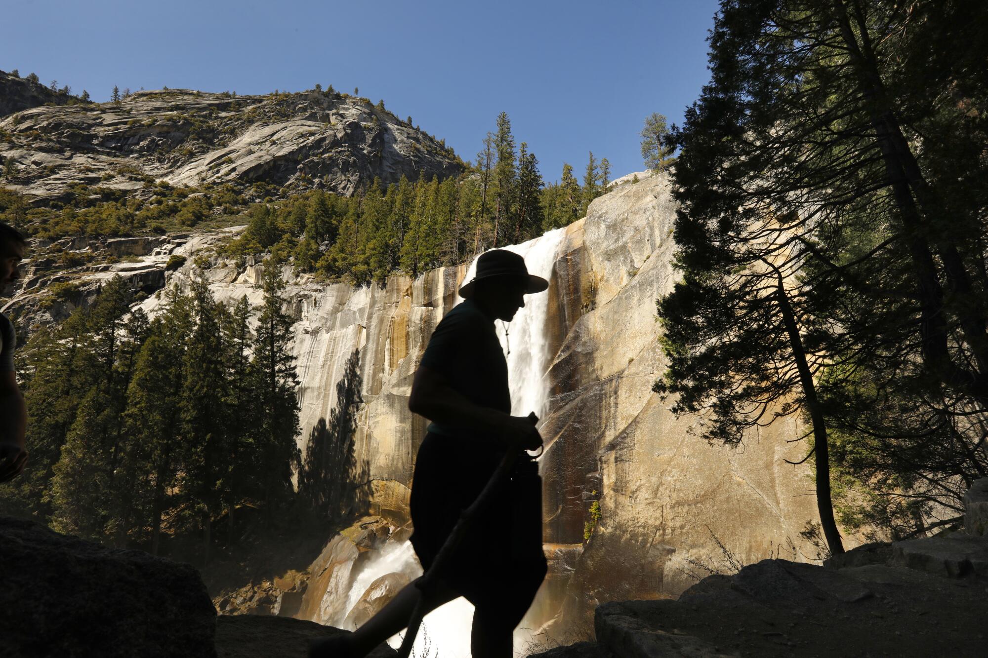 A hiker is silhouetted against a large waterfall