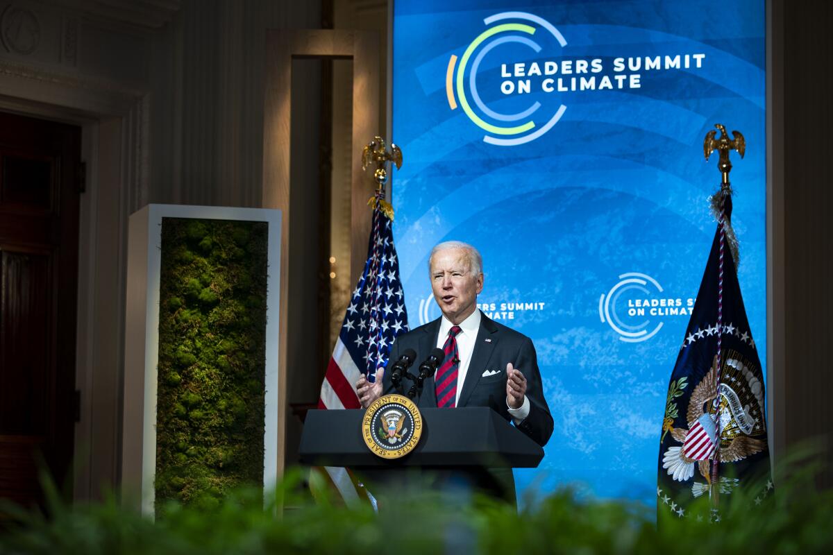 President Biden speaks before a backdrop reading Leaders Summit on Climate Change