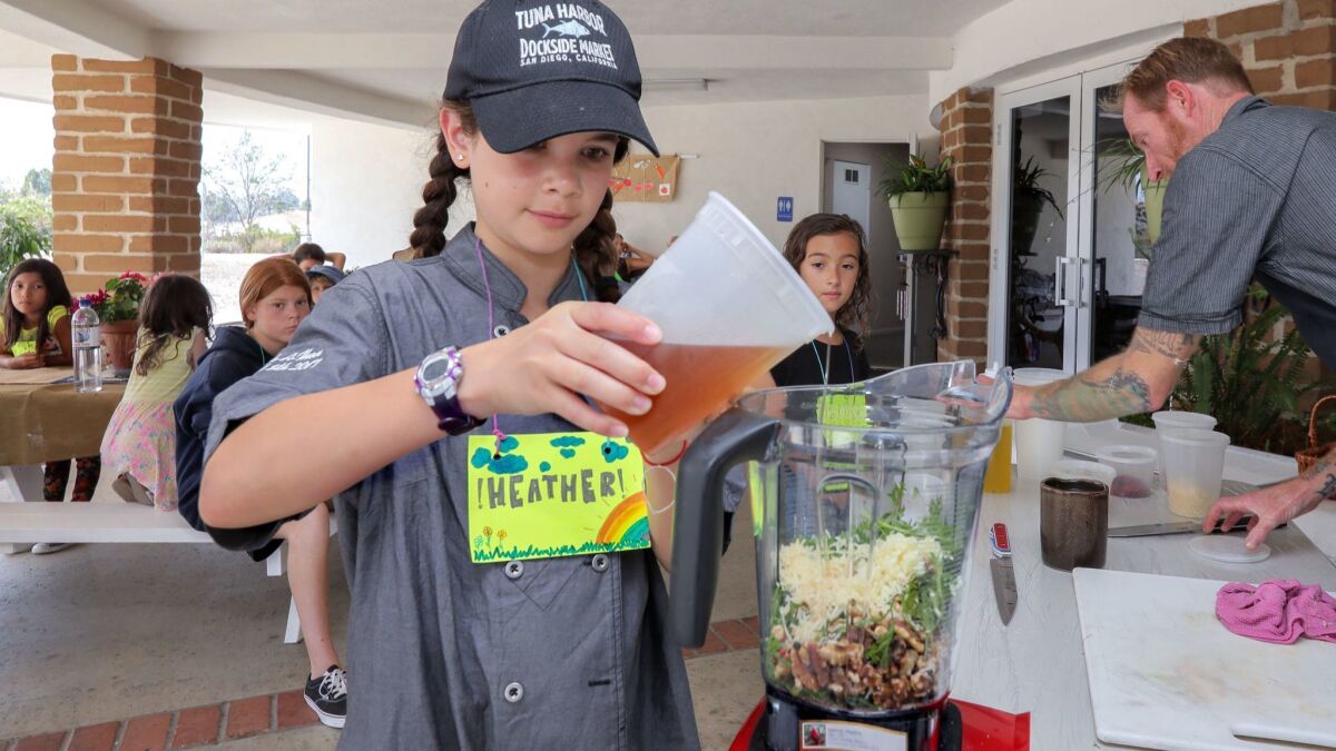 Heather Major, a participant of the Willow Tree Center, a sustainable living camp, pours flavored vinegar into a mixture to make pesto sauce during a sustainable cooking presentation by chef Davin Waite, at right.